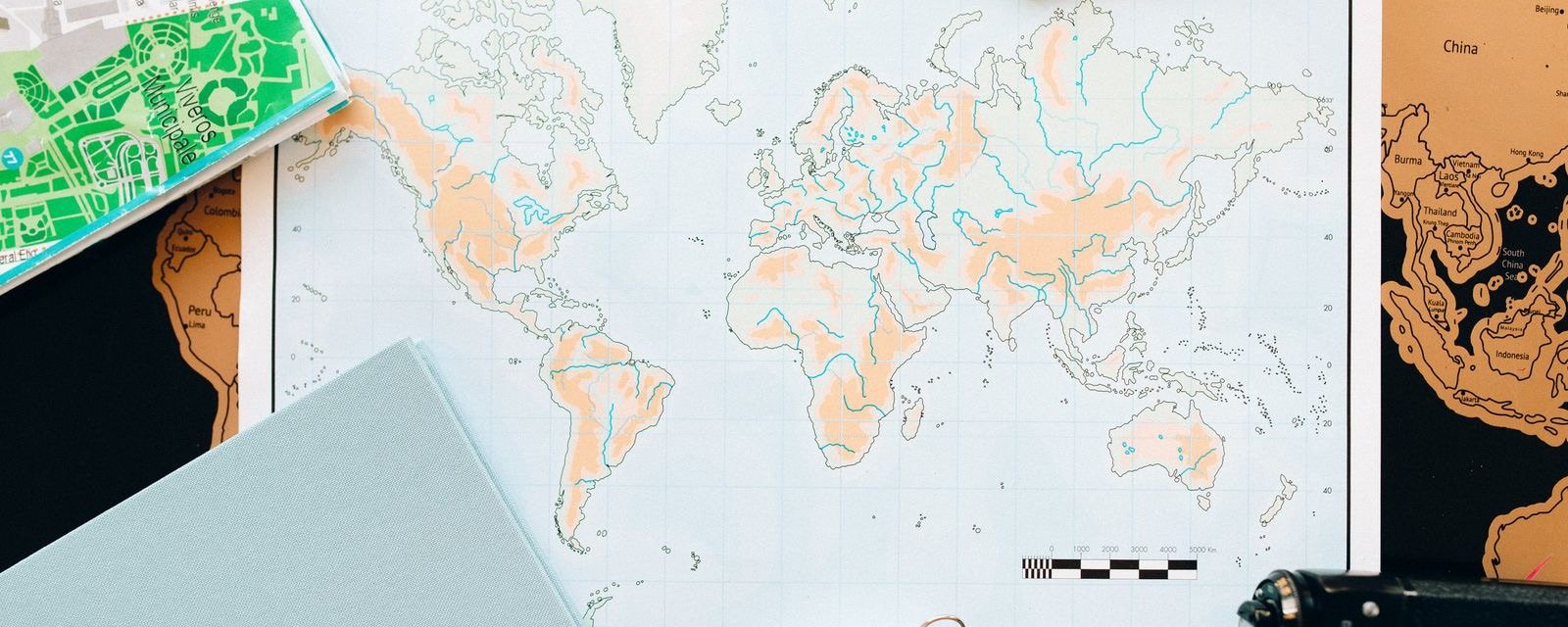 A world map with a notebook, compass and camera laid out for trip planning
