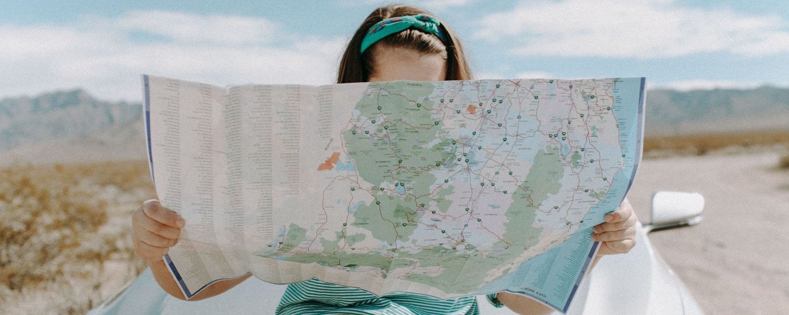 A traveller reading a large road map in front of a car in the desert