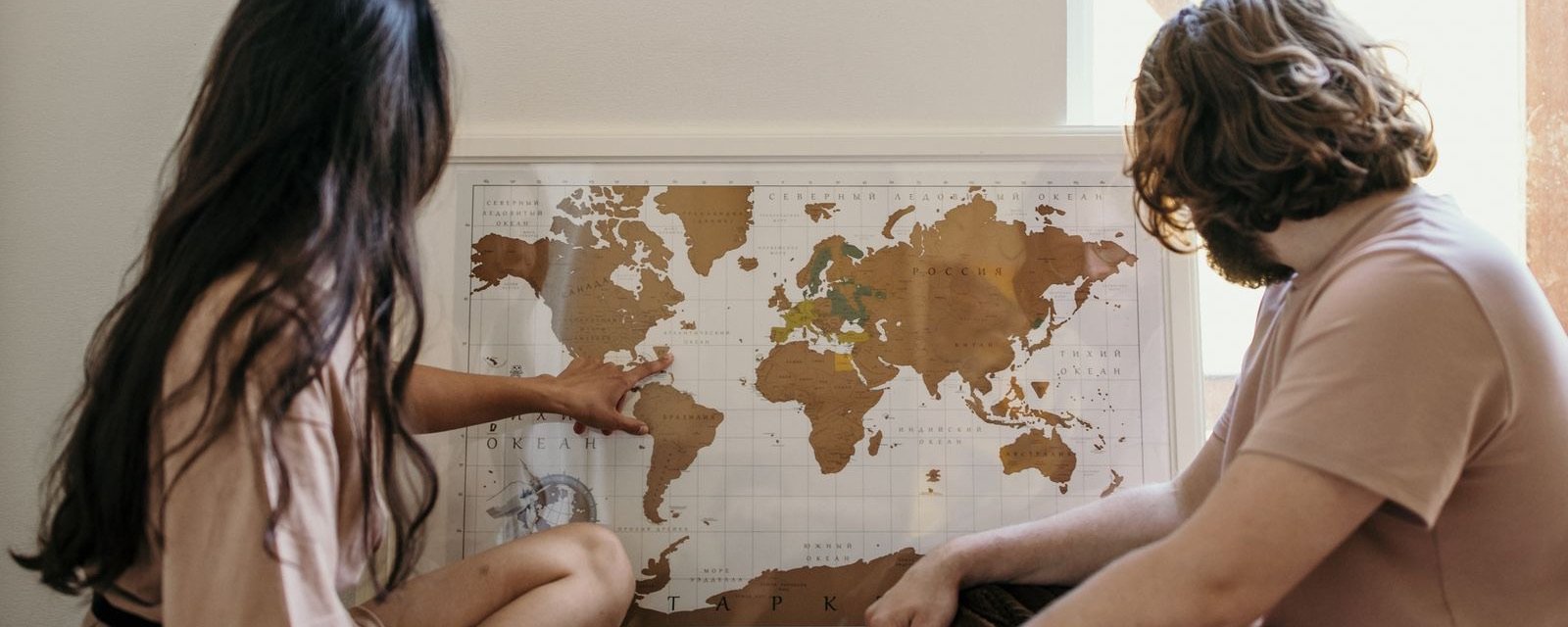 Two people sitting on the floor pointing at places on a world map